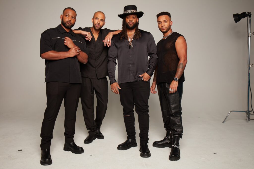 JLS play the Eden Project in the Eden Sessions 2024 in July 2024. Here they stand, all wearing black, against a white background, all four of them looking moody