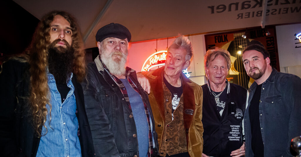 The members of rock band Atomic Rooster line up for a promotional image at the front of a rock club ahead of the Cornwall Rocks 2023 live music festival in Tencreek Holiday Park in Looe, Cornwall. The musicians stand side-by-side and just look cool for the best Cornwall rock music festival in 2023. One member has a long white beard and black hat