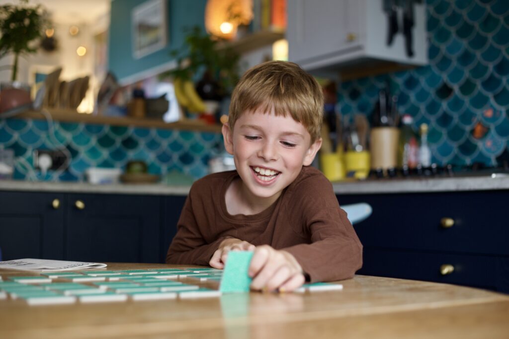 A young boy plays the Cornwall Memory Game at his kitchen table. He smiles as he picks up one of the blue-backed cards