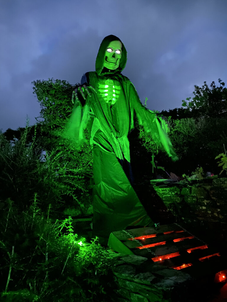 A skeletal figure is shrouded in green light at night at the Halloween at Trethevy 2023 display in Cornwall. There are also hellish red lights in this spooky scene