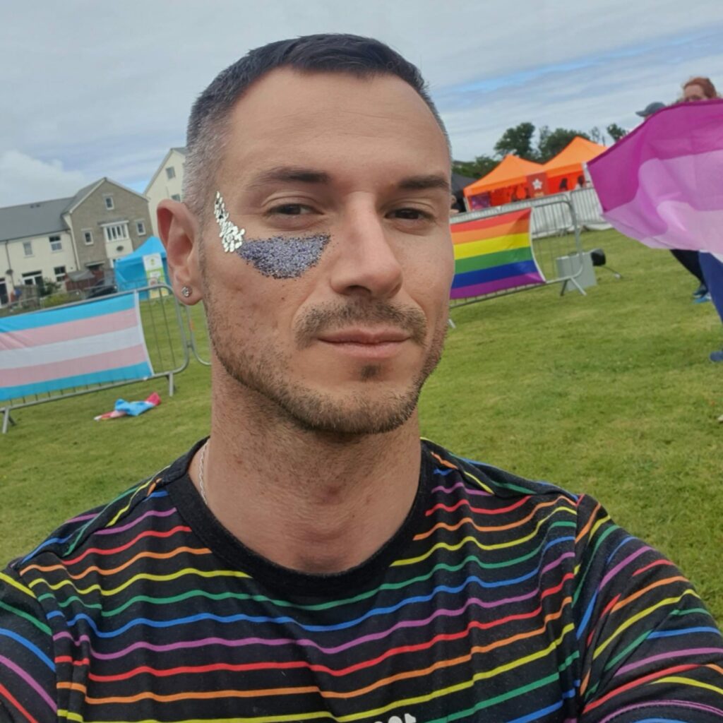 Matthew Kenworthy Gomes with a cute silver face painting image under his right eye. He is the chief executive of Cornwall Pride and poses here in a rainbow sweater