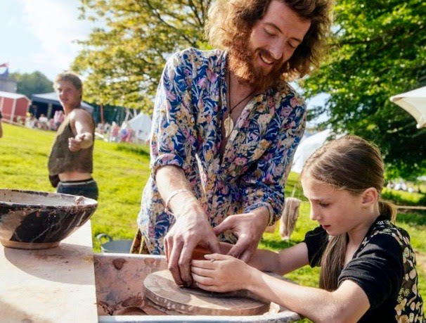 A man and a young girl make pottery together in a field in Cornwall for Swordfest 2023. The pottery wheel is ancient
