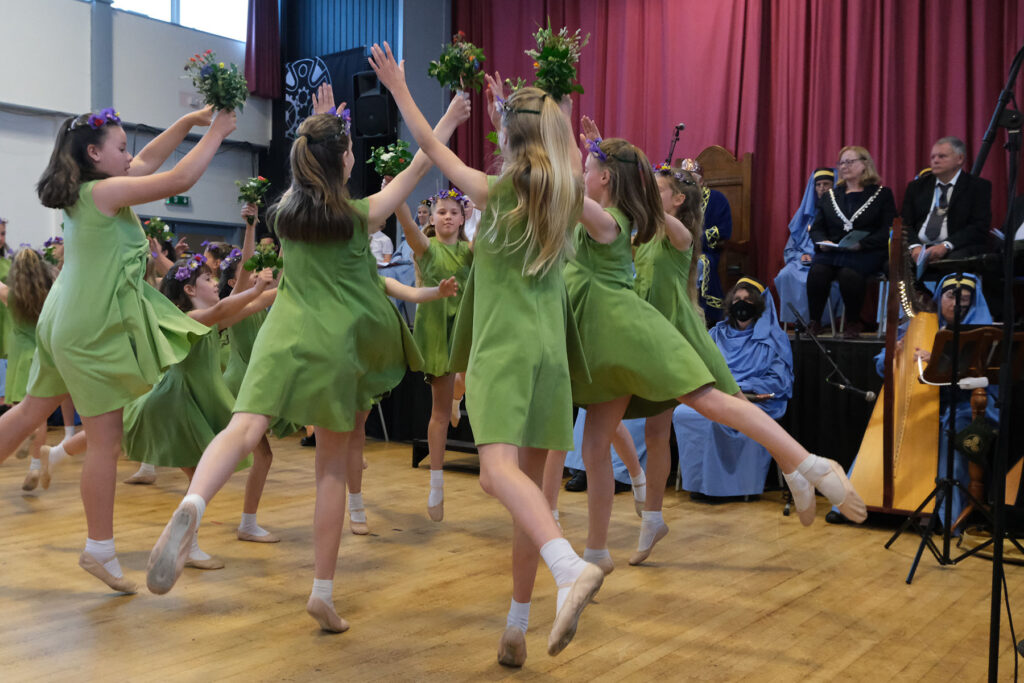 Young girls dressed in green dresses dance with wreaths inside a hall at Gorsedh Kernow. They will dance at Gorsedh Padstow 2023 as part of the bard's celebrations