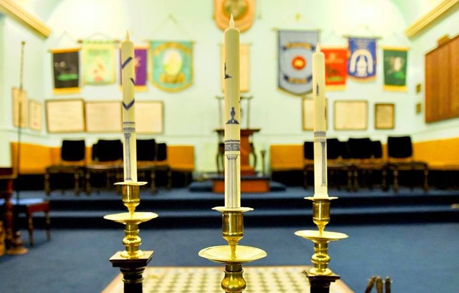 Three symbolic candles stand at the head of a chequered floor panel at the Redruth Masonic Lodge in Cornwall. In the distance are chairs, banners and plaques inside the masonic centre which enjoys an open day on Saturday 9 September 2023